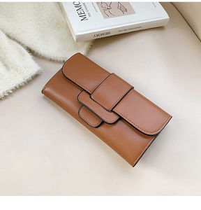 Detail of a brown leather envelope wallet featuring decorative overlapping straps and black trim
