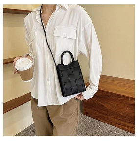 Detailed view of a black woven mini crossbody bag worn by a model in a modern home setting