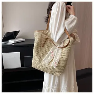 Detail view of woven straw tote bag featuring pink floral embroidery and lace ribbon trim