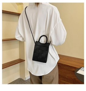Minimalist black woven leather crossbody phone bag shown being worn by a model in a room