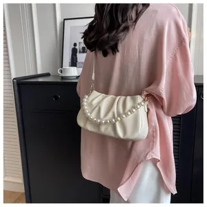 Detail of cream pleated cloud bag with pearl handle and leather strap on model
