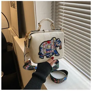 Détail de la broderie éléphant et de la bandoulière fleurie sur un sac en cuir beige