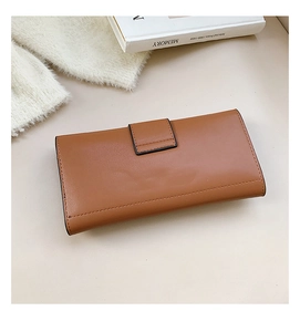Detail of caramel brown minimalist long wallet with flap closure on a white book