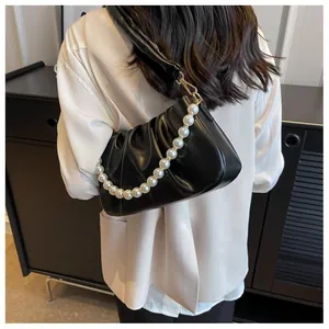 Detail of black pleated cloud bag with elegant pearl strap and gold hardware accents