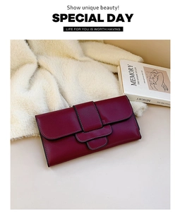 Detail of burgundy leather wallet with buckle strap and edge stitching on soft fabric