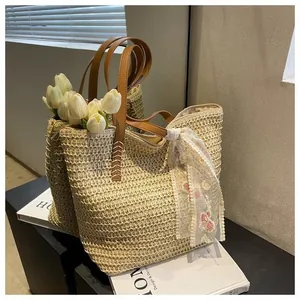 Detail of straw tote bag featuring brown leather handles and pink floral lace scarf decoration