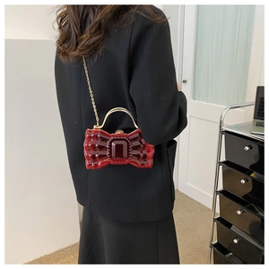 Détail d'une pochette nœud rouge avec texture facettée et poignée dorée
