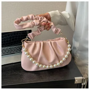 Close-up of pink ruched cloud bag with decorative pearl chain on a wooden desk