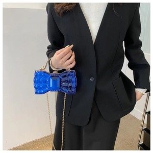 Détail d'un sac à main bleu translucide en forme de nœud avec chaîne dorée et anse