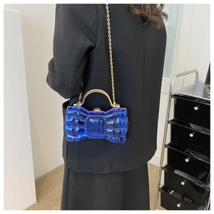 Pochette nœud en acrylique bleu avec poignée dorée portée à l'épaule par un mannequin