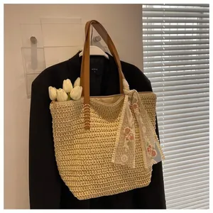 Detail of hand-woven straw tote bag with brown leather handles and floral lace ribbon