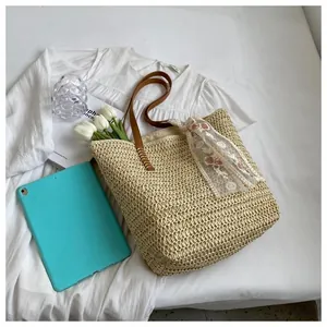 Top view of woven straw tote bag with brown handles and floral scarf on a white surface