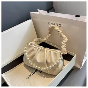 Detailed view of cream pleated bag with pearl chain handle in luxury gift packaging