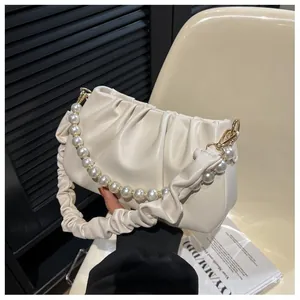 Detail of off-white ruched cloud bag with pearl strap and gold hardware on a chair