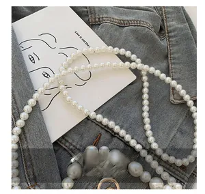 Détail de la bandoulière décorative en perles blanches pour sacs sur fond en denim