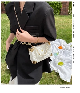 Detail of white quilted box bag with pearl handle and golden floral clasp on grass