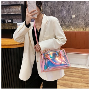 Iridescent PVC tote bag with pink leather straps worn over a white casual suit