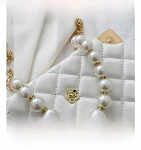 Detail view of white quilted bag with camellia metal ornament and pearl handle