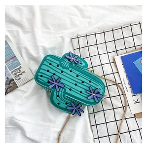 Detail of green cactus-shaped handbag with 3D purple flowers and a golden chain strap