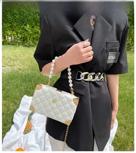 Detail of white quilted crossbody box bag with pearl handle and golden floral logo