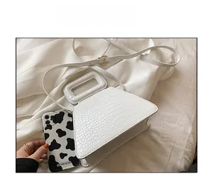 White crocodile pattern mini handbag with cutout handle shown next to a phone for size comparison