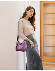 Detail view of purple multi-zippered crossbody bag in soft leather on a model