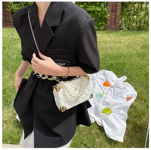 Close-up of white quilted box bag with gold metal corners and pearl handle detail