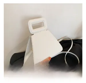 Detail shot of white crocodile embossed trapezoid handbag with cutout handle and shoulder strap