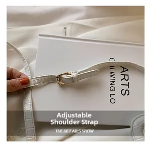 Detail of adjustable white crocodile embossed shoulder strap with golden metal buckle