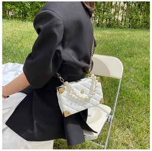 Detail of white quilted crossbody bag with pearl handle and golden metal corners