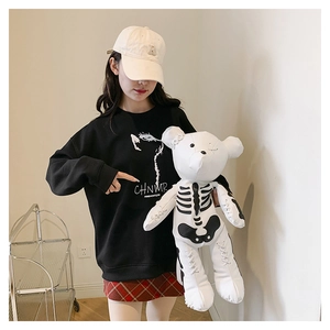 Detail of streetwear outfit with black sweatshirt, plaid skirt and white skull teddy bear