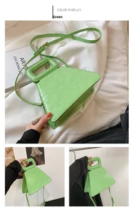 Detail view of green crocodile texture triangular handbag with a hollow handle and strap