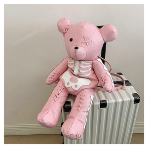 Pink bear backpack with white skeleton pattern on textured leather, resting on luggage