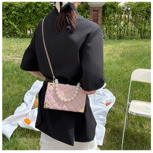 Pink quilted box bag with pearl handle and metal corners shown in outdoor picnic setting