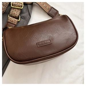 Gros plan sur un sac bandoulière marron foncé, texture litchi et sangle géométrique