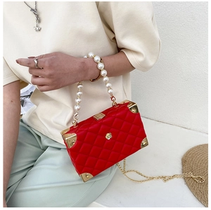 Detail of red quilted box bag featuring pearl handle and gold floral clasp accents