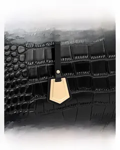 Detail of black crocodile texture leather bag with a rotating gold shield charm hardware