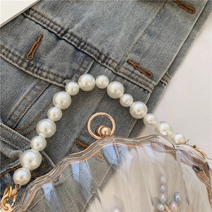 Détail d'un sac transparent en forme de coquillage avec une anse en perles et décor marin
