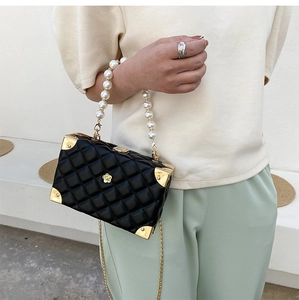 Close-up of a black quilted box bag featuring pearl handle and gold chain shoulder strap