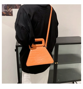 Detail view of a bright orange crocodile texture trapezoid handbag worn as a crossbody bag