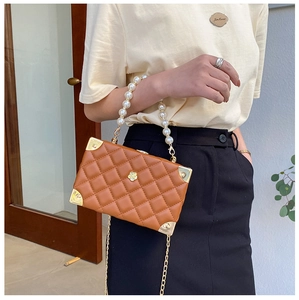 Detail of brown quilted box bag featuring pearl handle and gold metal corner protectors