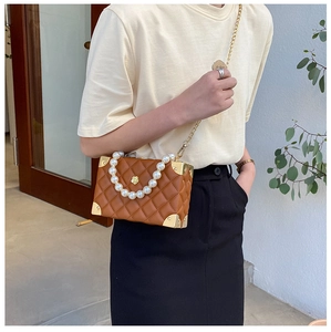Close-up of brown quilted box bag with decorative pearl handle and gold chain strap