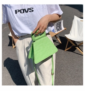 Detail of lime green faux leather trapezoid bag with crocodile texture and cutout handle
