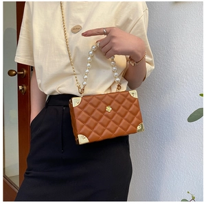 Close-up of caramel quilted crossbody bag with pearl handle and golden corner details