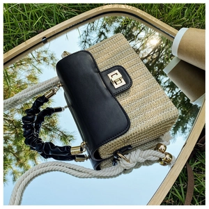 Detail of woven straw handbag featuring black leather flap and decorative hemp rope handle