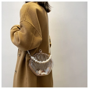 Détail d'un sac coquillage en acrylique avec bandoulière perles sur un manteau