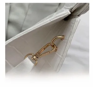 Detail showing high-quality light gold metal hook and crocodile pattern texture on a white bag