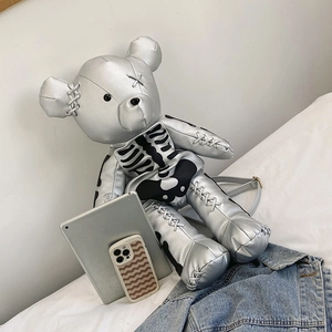 Metallic silver bear-shaped backpack with black skeleton print on a white bed