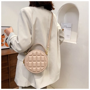 Detail of round quilted beige shoulder bag with golden hardware and textured finish