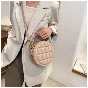 Detail of beige quilted round handbag with gold hardware shown in a stylish room